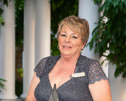 A middle aged woman with short hair smirks at the camera as she holds an award.
