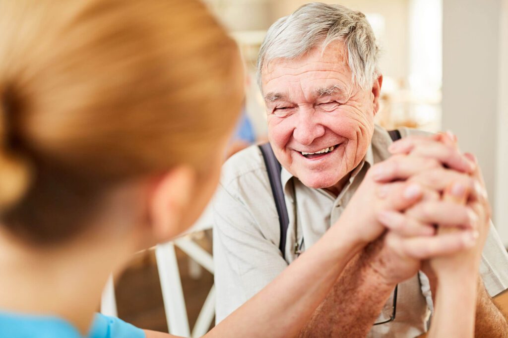 a elderly man holds the hands of a caretaker with a big smile, Memory Care at Montage Creek