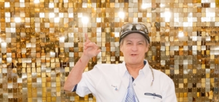Man stands in front of a gold backdrop and accepts an award