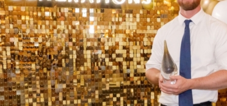 Man stands in front of a gold backdrop and accepts an award