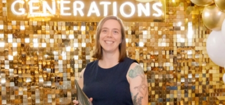Woman stands in front of a gold backdrop and accepts an award