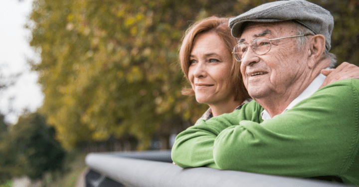 An elderly man in memory care looks off into the distance as a loved one puts their arm on his shoulder